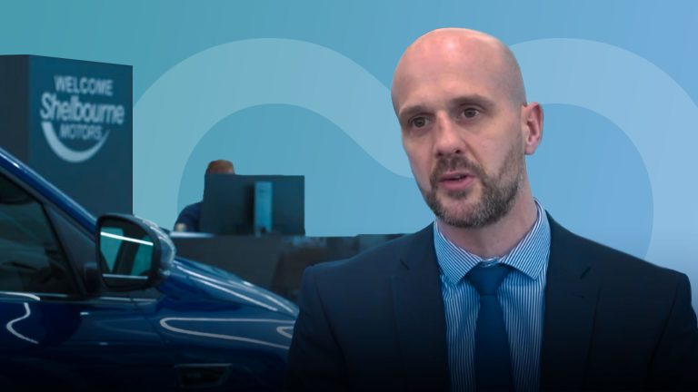 A man in a suit being interviewed on camera whilst sitting in a car dealership