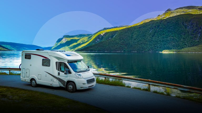 A motorhome is parked on a hill overlooking a serene lake and the beautiful hillside scenery.